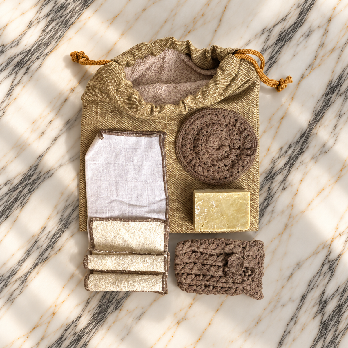 Ritual Hamam II karamel: el örgüsü pamuk disk ve sabunluk, ekru havlular, muslin bez ve doğal sabunun mermer üzerinde düzenlendiği hamam hediye seti.