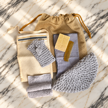 Ritual Hamam III Restore: açık gri el örgüsü pamuk disk, kese ve havluların tarak, doğal sabun ve wet bag ile mermer üzerindeki hamam seti görünümü.